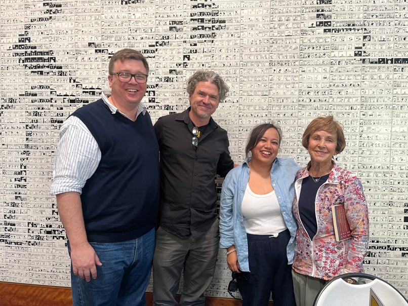 Authors Benjamin L. Clark, Dave Eggers, Susan Minichiello, and Jean Schulz stand together smiling in front of a ceramic tile mural at the Schulz Museum.