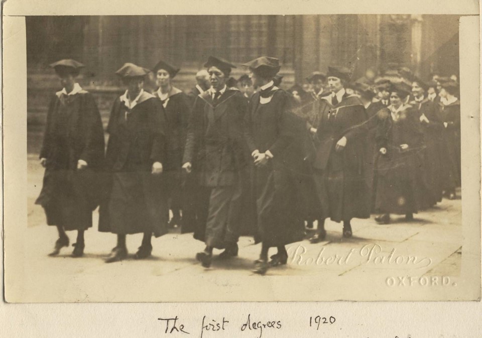 A black and white photo of walking in a group to receive their degrees in 1920. Wearing academic gowns and soft academic gaps. "The first degrees 1920" written at the bottom