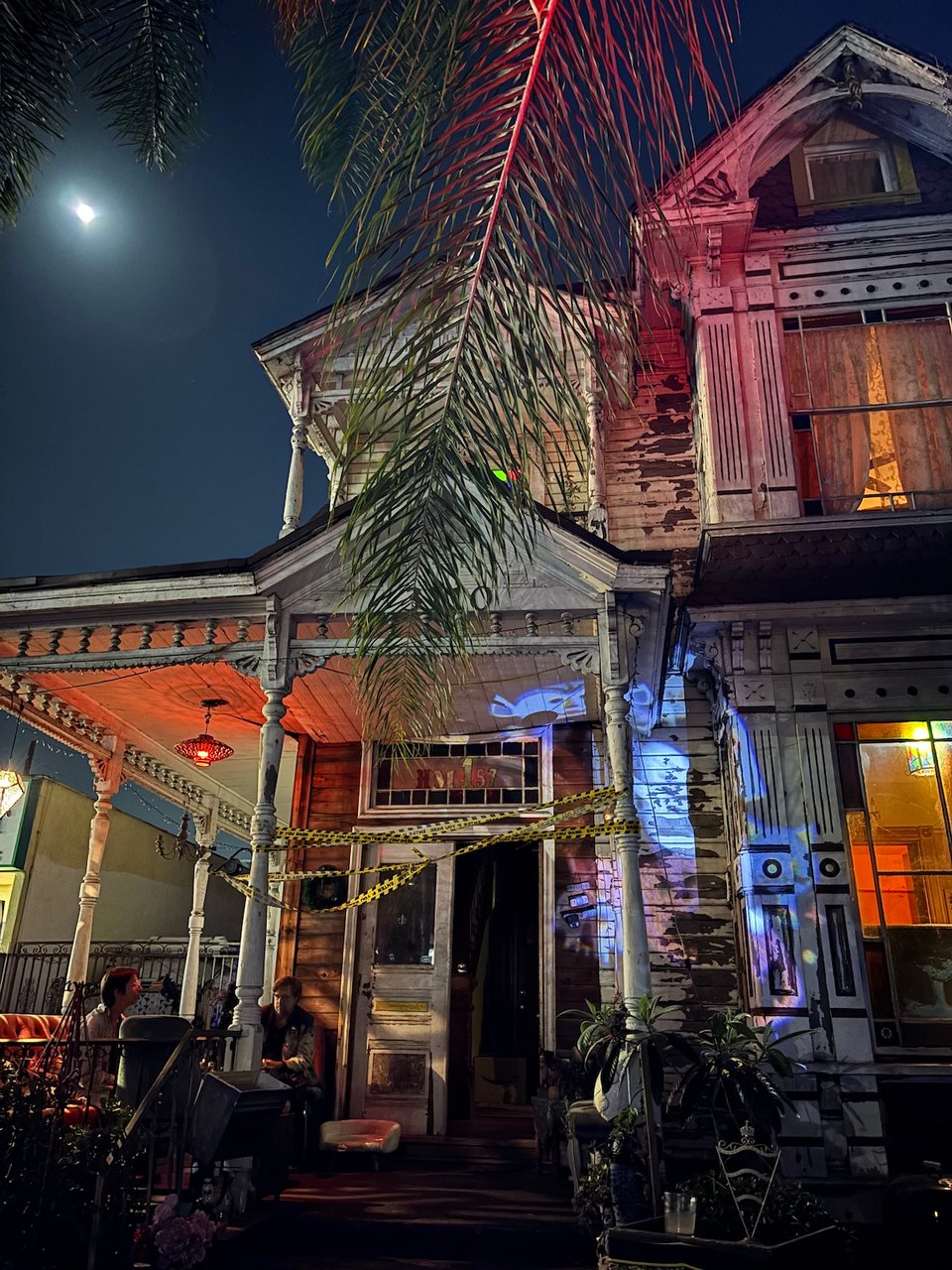 the front of a rather dilapidated victorian house decorated for halloween. the moon is visible behind it. very spooky.