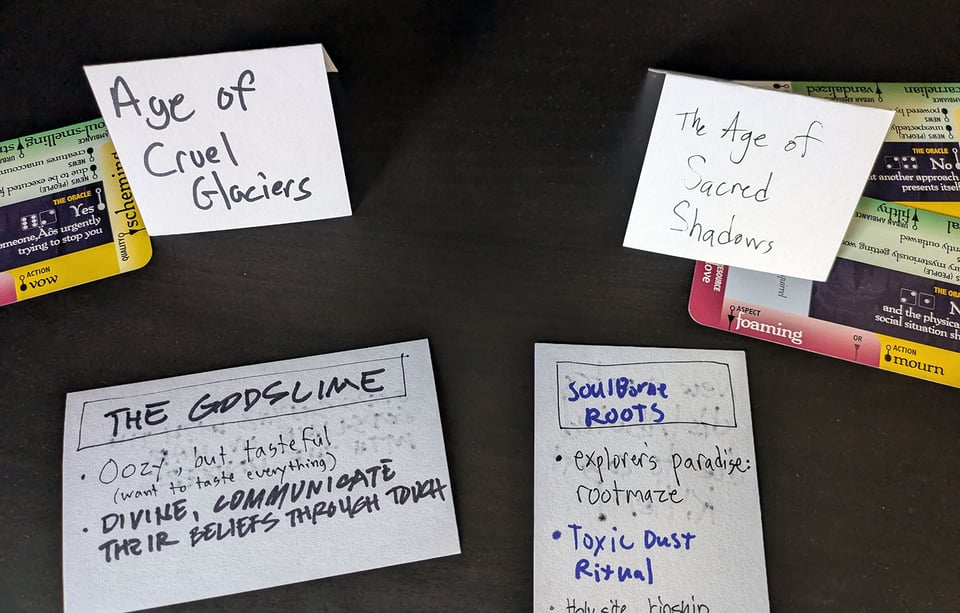 Index cards with prompts written on them, including "The Age of Cruel Glaciers" and "The Age of Sacred Shadows," as well as "The Godslime" and "Soulborn Roots."