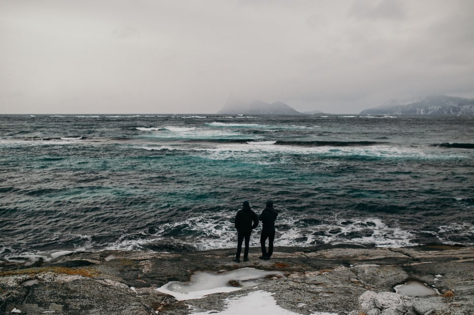 Ocean tinged with light and dark green, two people gazing at the water.