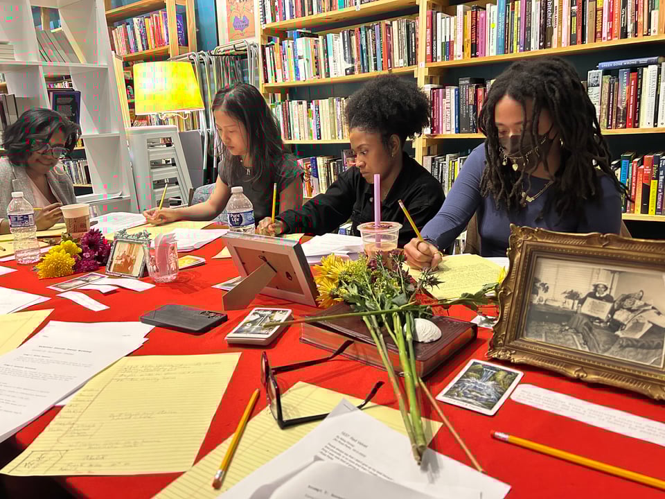 four people writing at a large table with a red table cloth