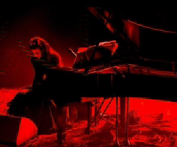 Photo of musician Diamanda Galas sitting onstage at her piano, with red light