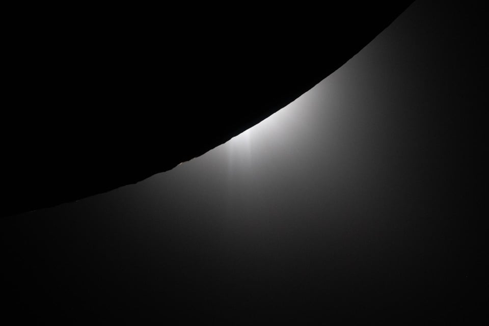 An eclipse of the sun behind the moon as seen from space, light from the sun peeking out behind a black circle on a slightly less black background