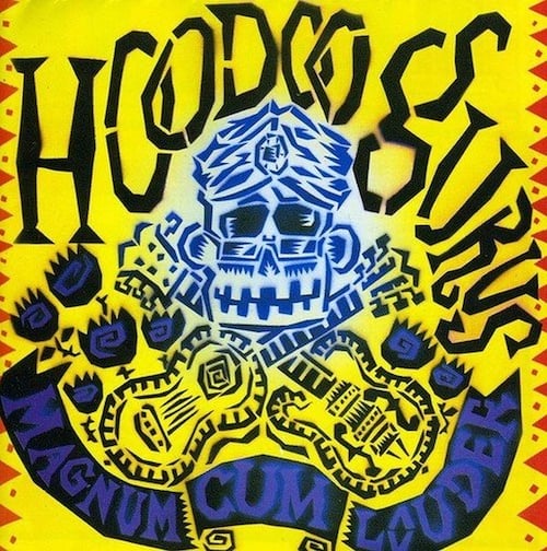 A blue drawing of a smiling monkey-skull-like face, with a jeweled-turban and glasses. Below the face are two crossed guitars, making a kind of "skull and bones" picture. Dotted around the gutiars are what I think are supposed to be black roses. A black banner across the bottom reads "MAGNUM CUM LOUDER." All of this is on a yellow background.
