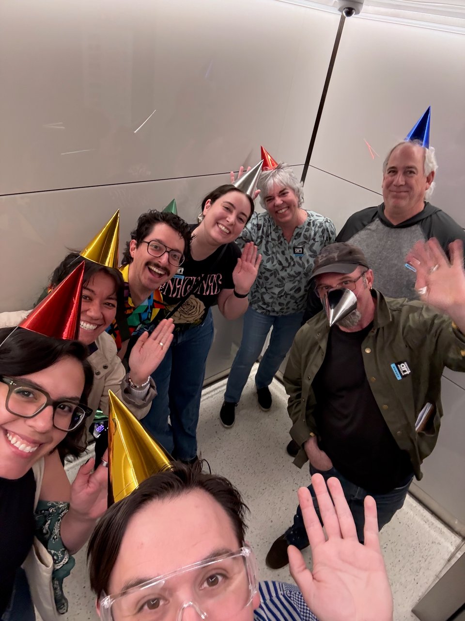 An elevator full of people wearing birthday hats.