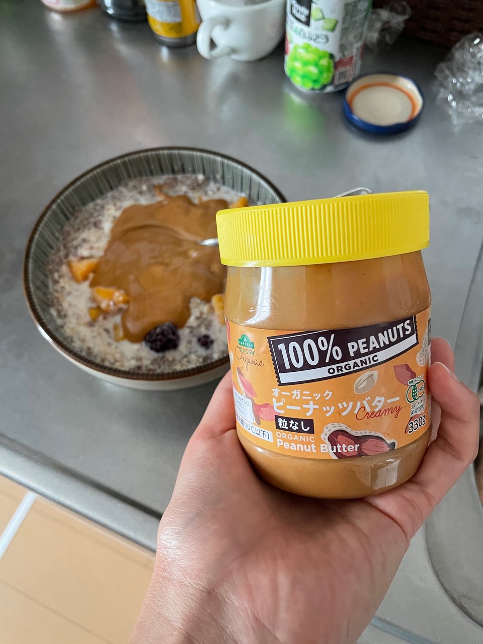 Image of a tiny ass pb jar fitting in the palm of a hand and a breakfast oatmeal behind it on the counter.