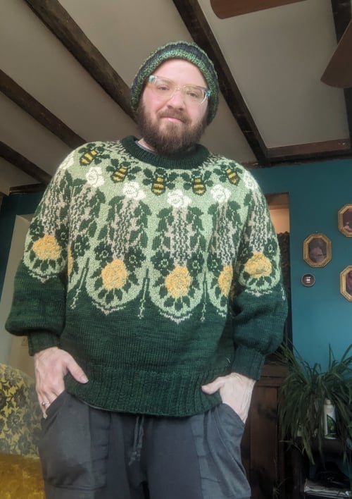 Me in my newly-knit sweater, an oversize one in mostly green, with detailed large scale colorwork of roses, bees, and leaves in yellow, white, different green, and tan
