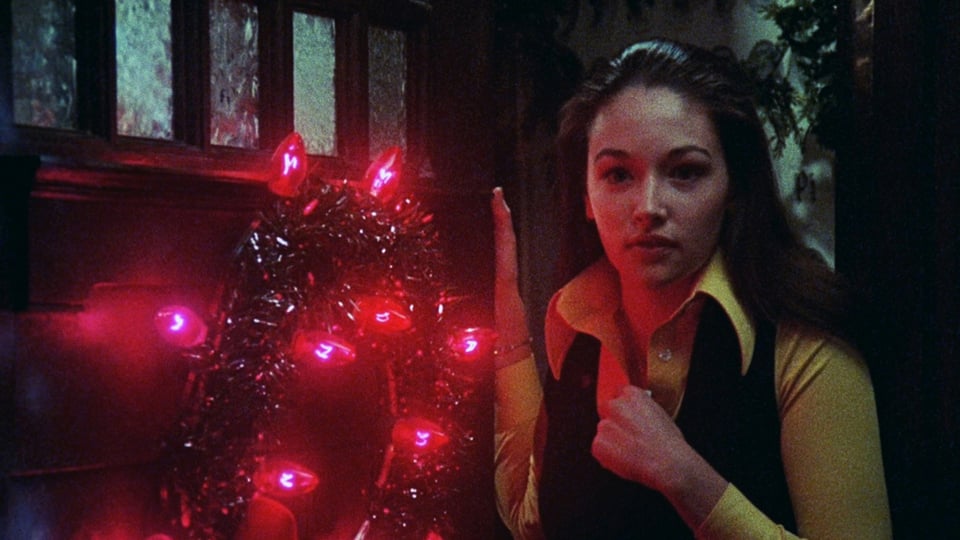 Olivia Hussey stands at the sorority house door, the wreath glowing red beside her, in Black Christmas.
