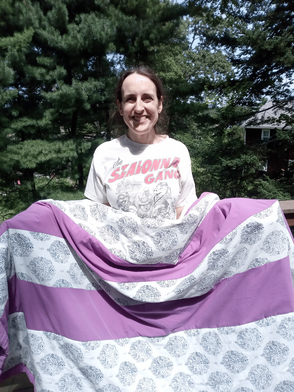 The author, a middle-aged white woman, holds the quilt out in the sun.