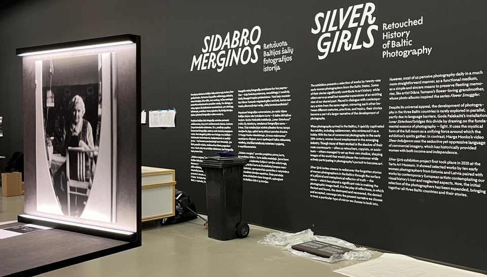 Photo of the Sidabro Merginos exhibition, still under construction. A black wall with white lettering in LTR Limited Grotesque.