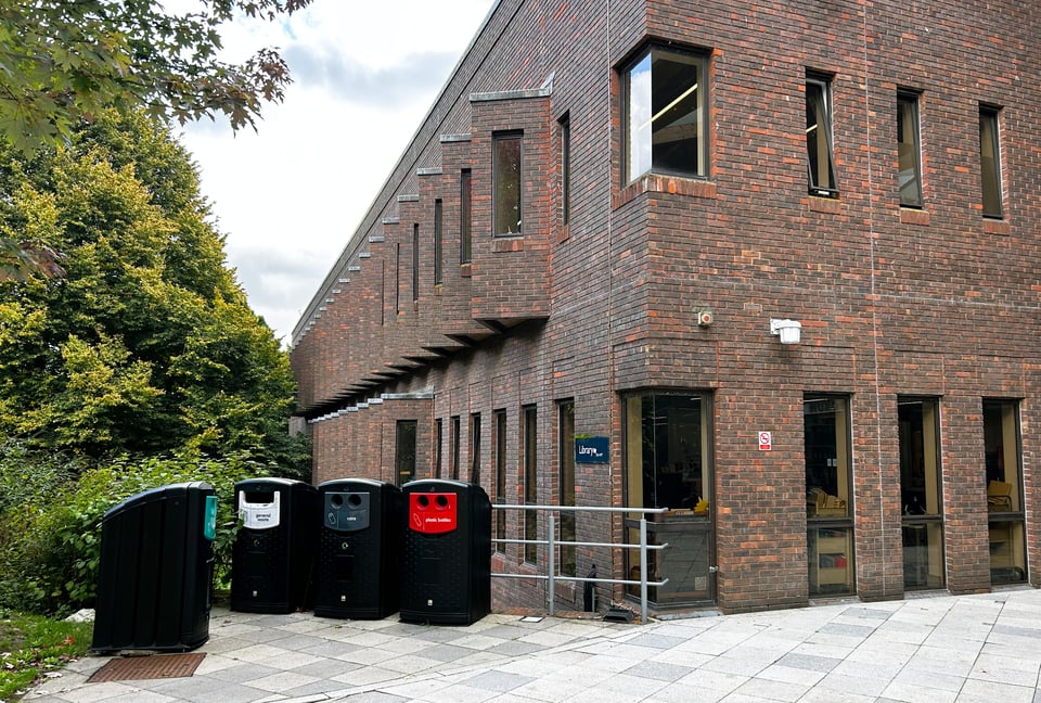 A dark red brick building with narrow windows. In the foreground, where there should be a great view of the eastern wall of the building, there are a huddle of recycling bins that look like they're having a chat. More description of the building is in the main email.