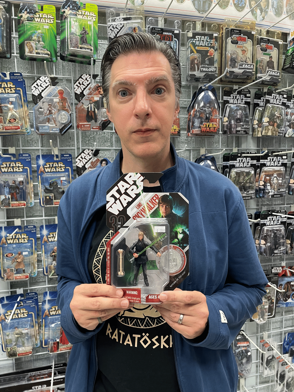 A middle-aged man proudly holds a Luke Skywalker action figure