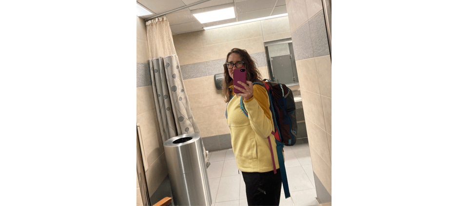 Katy in an airport bathroom mirror, wearing a yellow fleece and a backpack