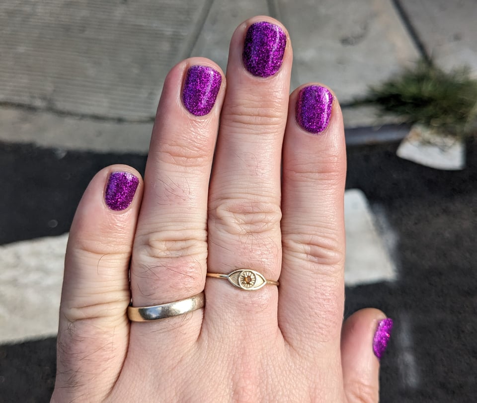 A closeup of a hand with nails painted in bright purple glitter.