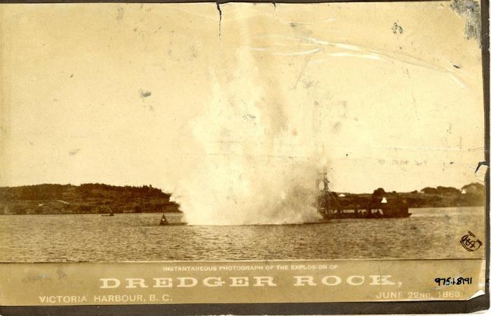 Sepia toned photograph. A column of water exploding from the ocean above a scow with machinery. Below,it reads "Instantaneous Photograph of the Explosion of Dredger Rock, Victoria Harbour, B.C. June 22nd 1888. "Instantaneous Photograph of the Explosion of Dredger Rock, Victoria Harbour, B.C. June 22nd 1888."