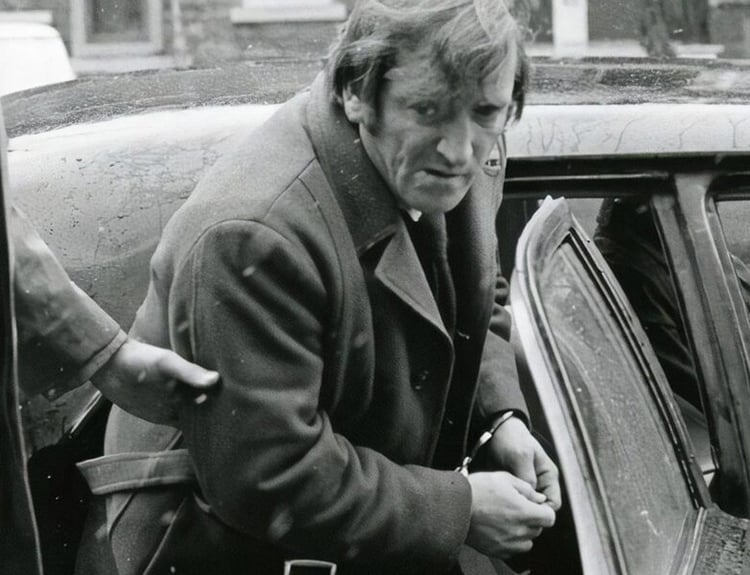 Actor Jean Lapointe, his hands in cuffs, being pushed into the rear of a car, in Les Ordres