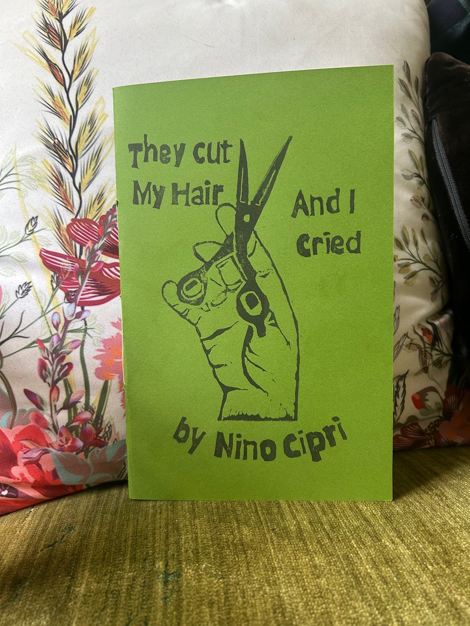 A half-page zine titled "They Cut My Hair And I Cried." The cover is green and shows a lino print of a hand holding a pair of hair-cutting shears.