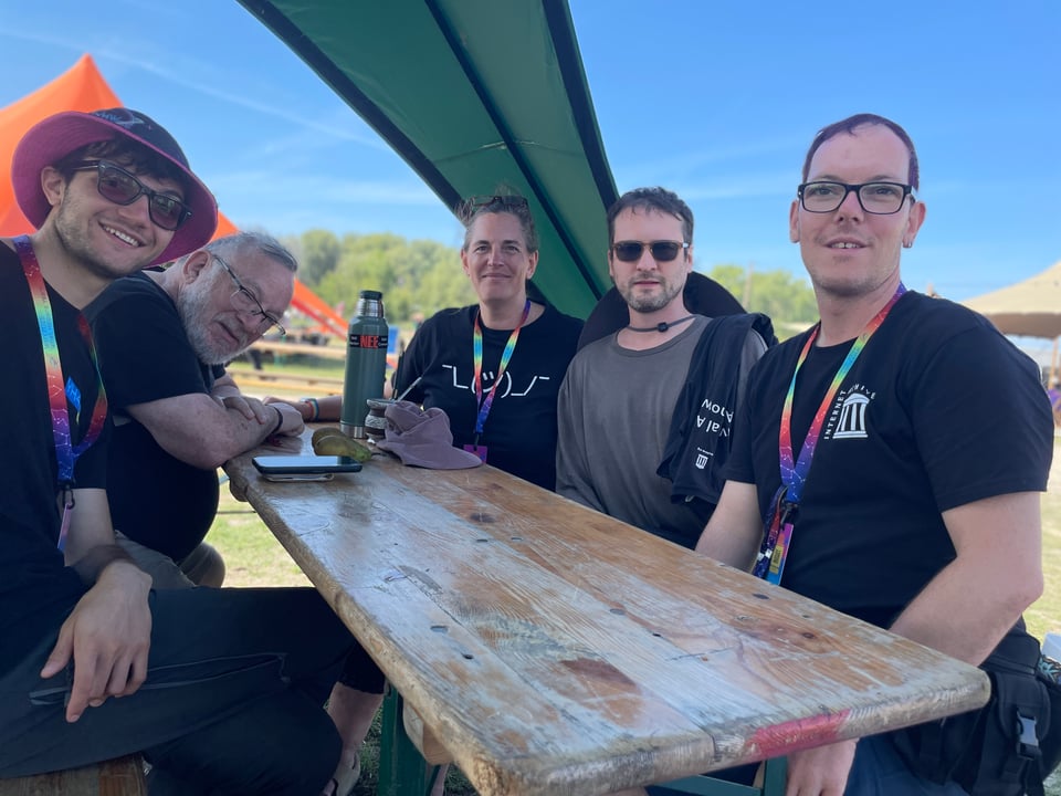 Five people around a picnic table under a green tent.