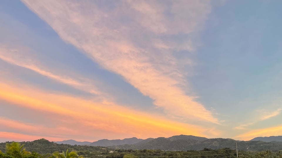Photo of yellow and pink straight clouds across the sky above a mountain landscape