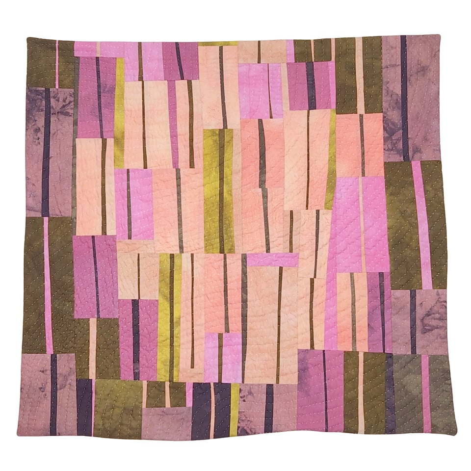 Photo of Sarah Atlee’s patchwork quilt titled Arabesque I. The quilt is made from hand-dyed fabrics in pink, orange, grey, purple, and yellow green.