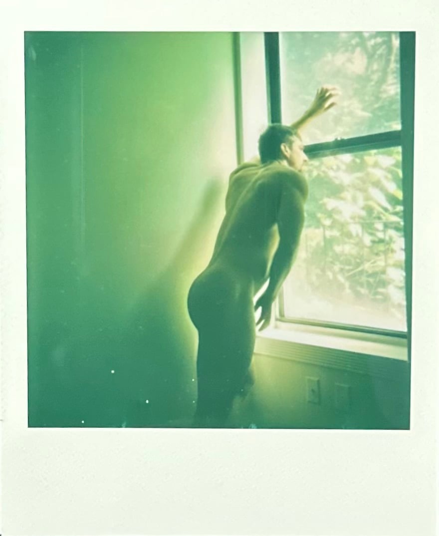 naked man stares out the window polaroid