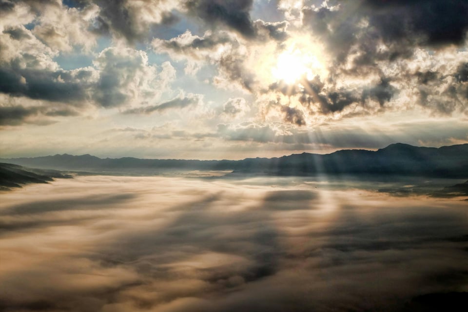Stock image of sunlight breaking through the clouds as it overlooks a darker landscape.