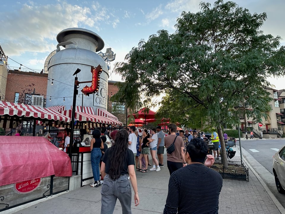 A crowd of really tiny people standing around a regular size jug of milk.