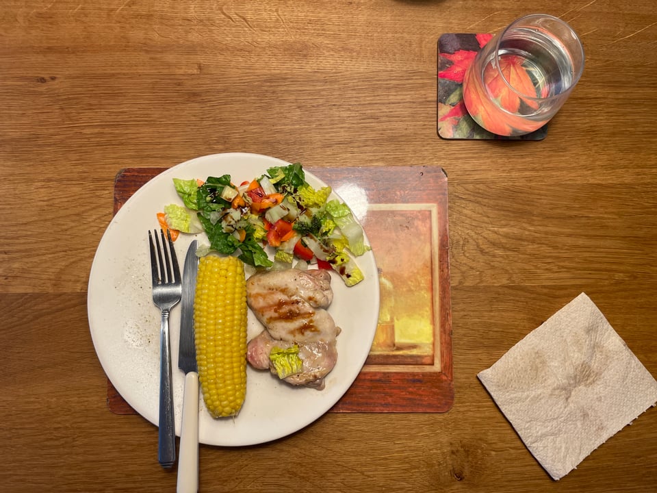 Plate of grilled chicken, salad, corn on the cob and a glass of water.