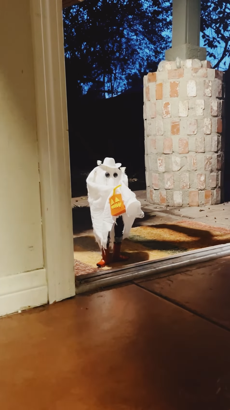 A small marionette puppet on a doorstep. The puppet is a trick or treater dressed as a ghost with a cowboy hat.