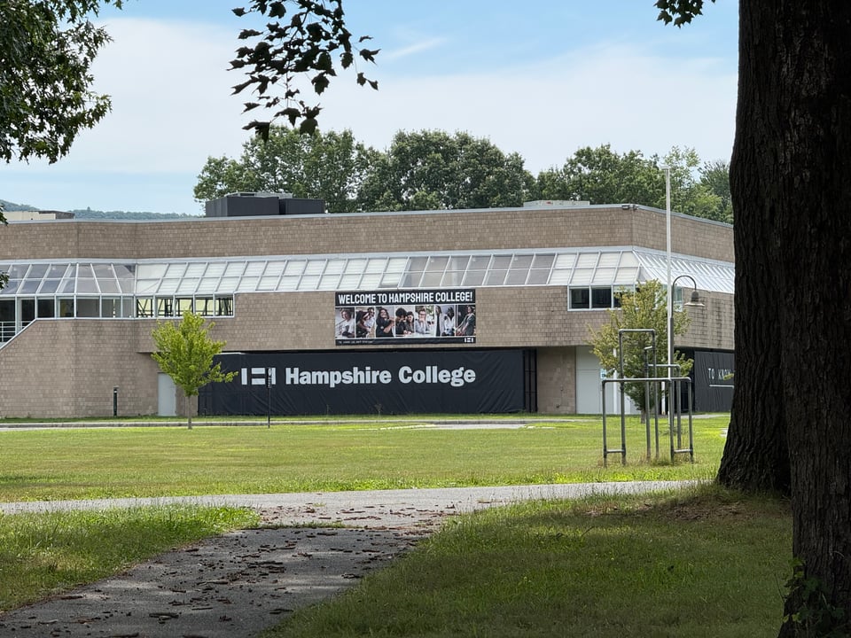 longer-range photo of a building with a perimeter of windows. There's a banner that reads, "WELCOME TO HAMPSHIRE COLLEGE," which is sad, because the place is shutting down at the end of 2026.