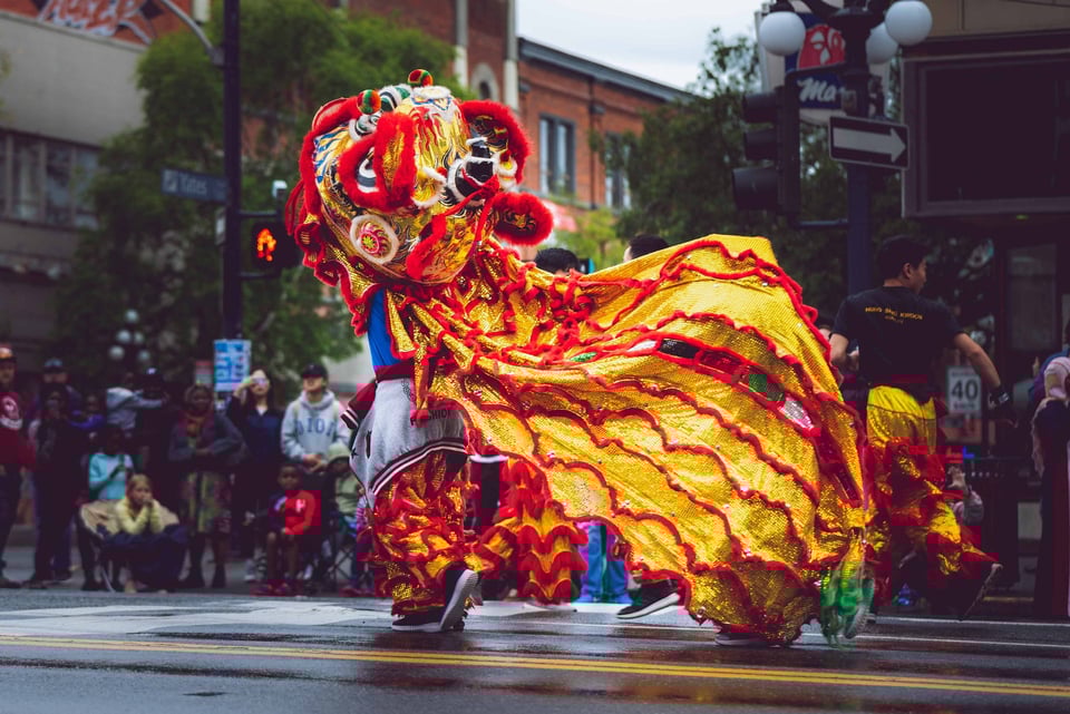 Lion dancer festooned in red and gold on a wet city street.
