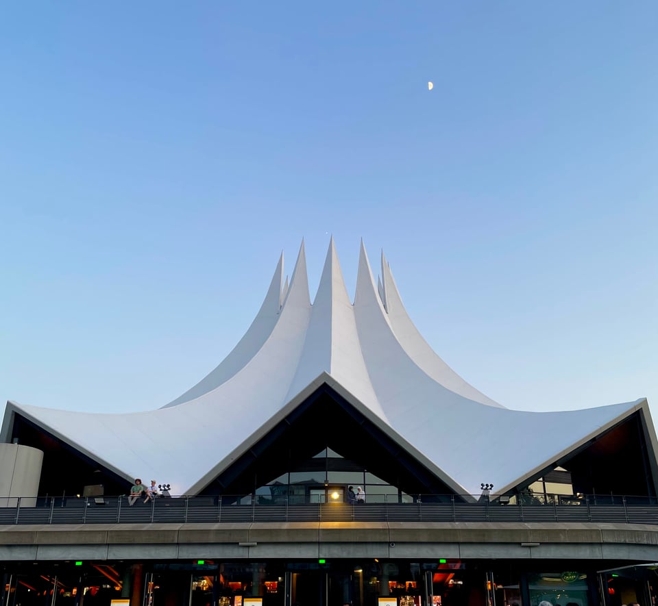 Prominently shows the Tempodrom, in Berlin, in the foreground. Taken from the ground below, with clear evening sky in the background, with a small half-moon