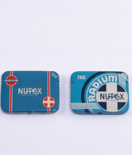 Colour photograph of Nutex condoms. Image shows the front of two metal cases that both have 'Nutex radium condoms' printed on them in different designs.