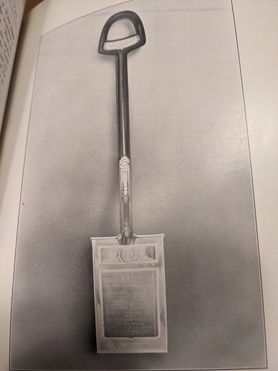 A black and white photograph from a book, featuring a silver spade with the seal of New York City and text honoring George B. McClellan
