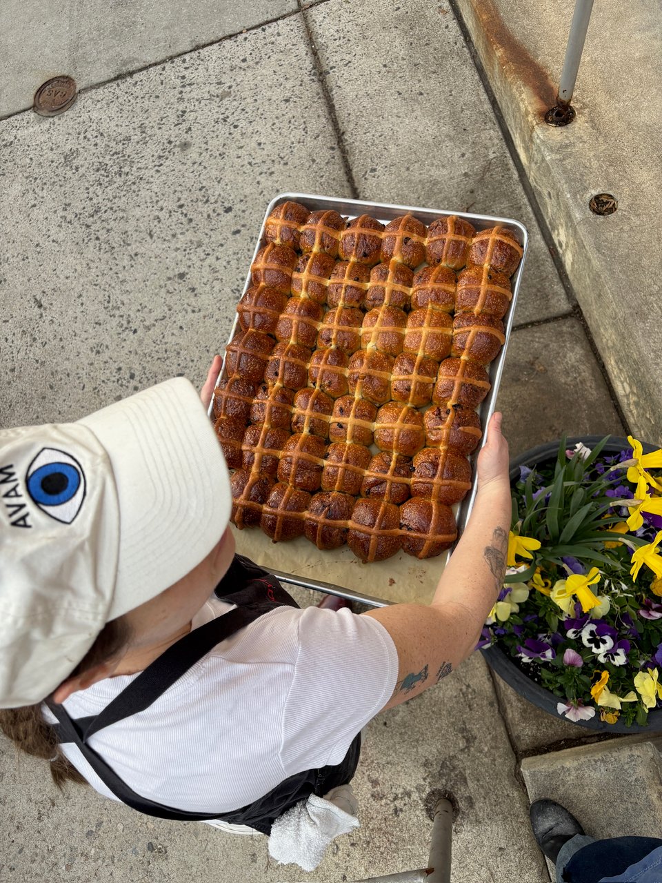 Woman in apron holding sourdough hot cross buns over a bed of flowers