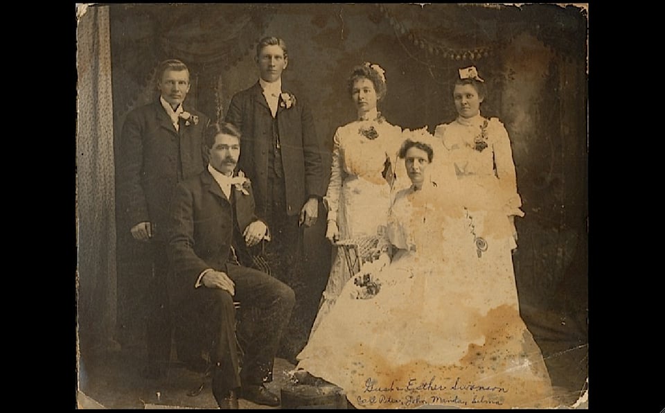 Three men wearing fancy suits and corsages, three women wearing fluffy white dresses. Everything is sepia and old timey.
