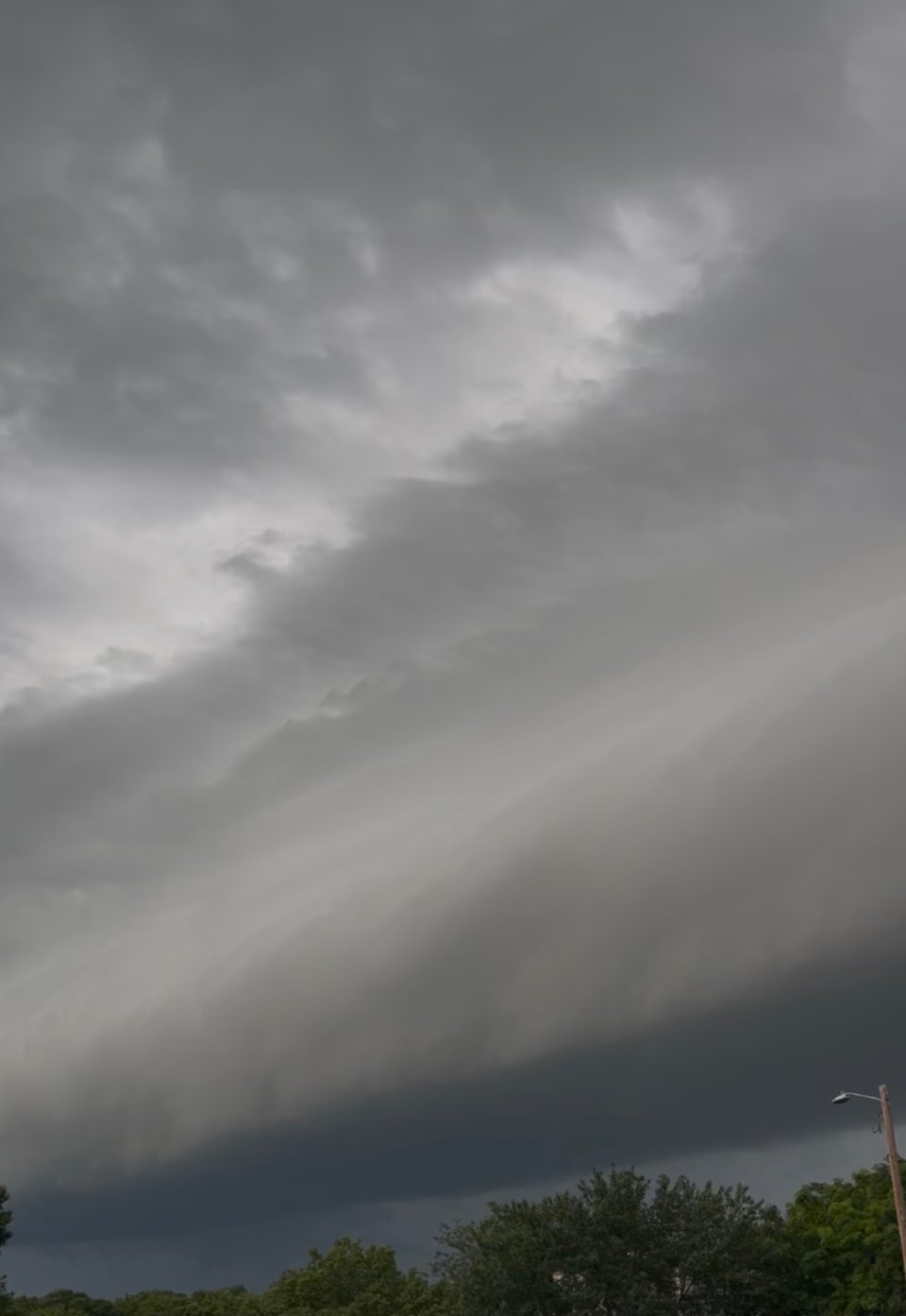 photo of a storm front rolling in, with a heavy band of dark gray hovering just over a line of green trees