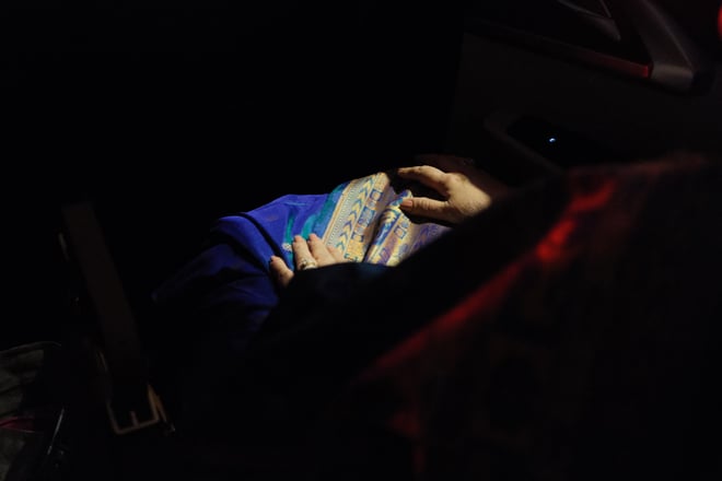 Photo of a woman's lap with some light falling and illuminating her sari and hands ever so slightly.