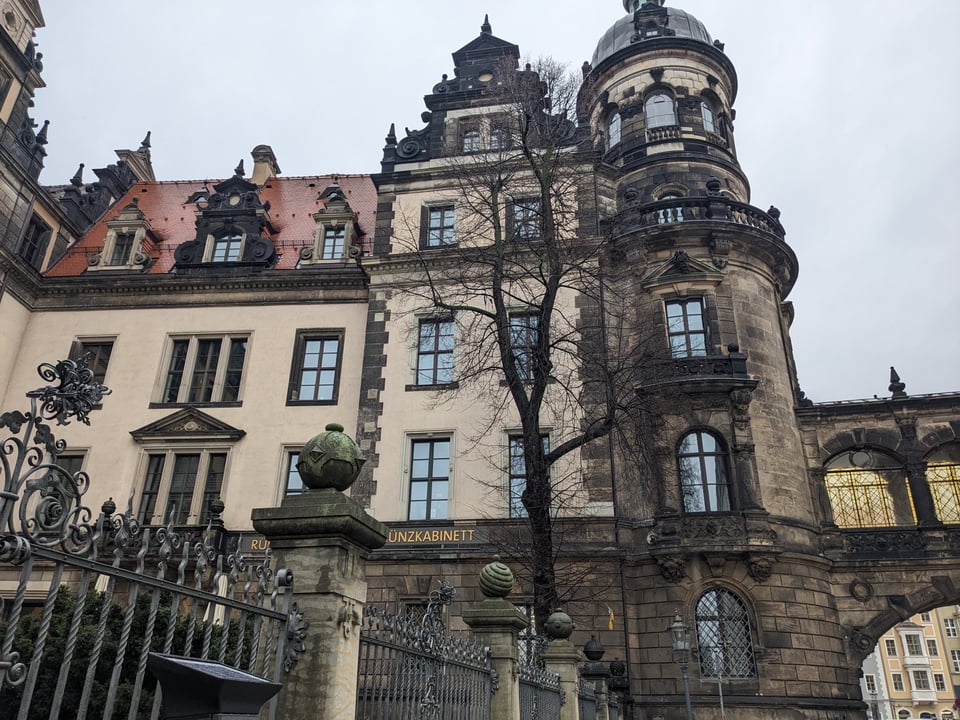 The Royal Residence, with an obviously rebuilt section (clean tan walls) juxtaposed with older, original pieces of the structure (the tower at the edge, parts of the foundation, some walls and some window and roof elements). The fence in front looks mostly original.