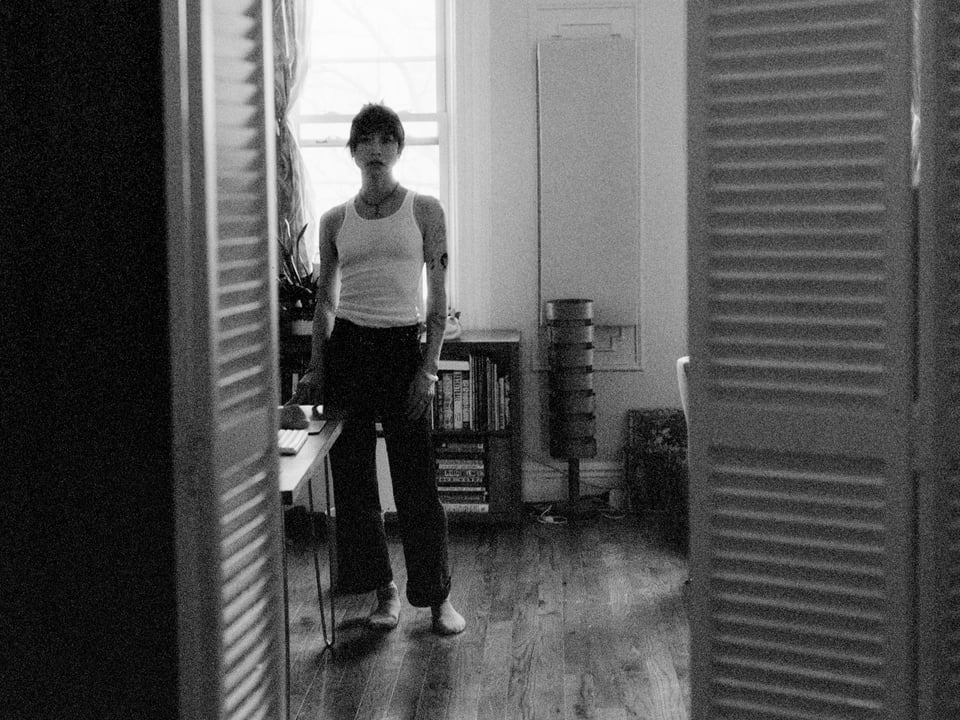 ohyung stands by her desk in her studio. there is a wood floor in an old nyc townhouse apartment and the photo is framed with a door on each side in the foreground.