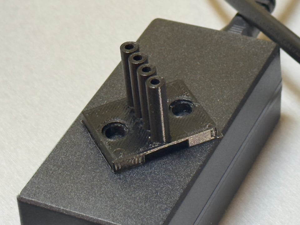 Black 3D printed bracket with tubes sitting on black power transformer
