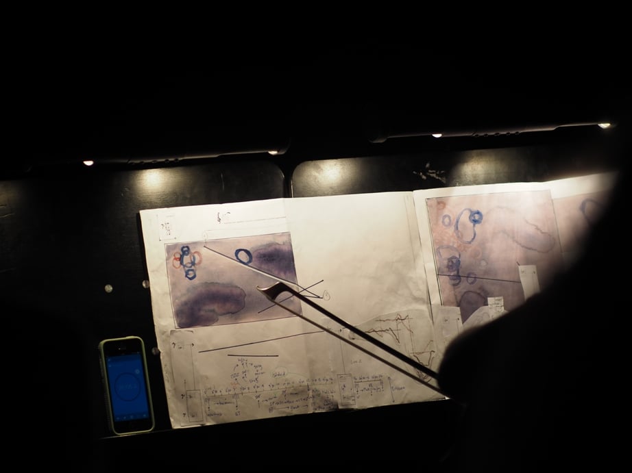 Sheet music on a music stand. In place of typical musical notation are what look like abstract water colors in purple and blue.