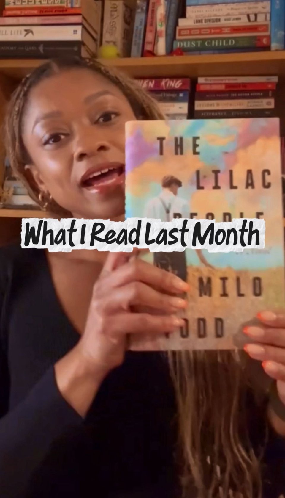 Video screenshot of me speaking while holding up the book The Lilac People by Milo Todd so that the cover is visible. The background shows bookshelves filled with stacked books. Overlay text across the centre reads “What I Read Last Month.”
