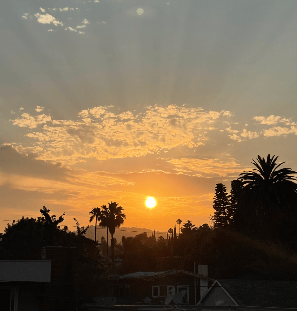 The sun peeks out from a cloud, glowing at sunset in Los Angeles