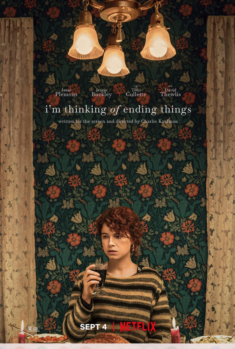 A poster for the movie I'm Thinking of Ending Things. Jessie Buckley sits in contemplation holding a glass of wine in front of a wall of flower wall paper.