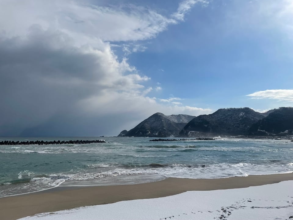 A snowy beach. The right side of the sky is sunny and clear, and just to the left is a thick veil of spooky clouds.