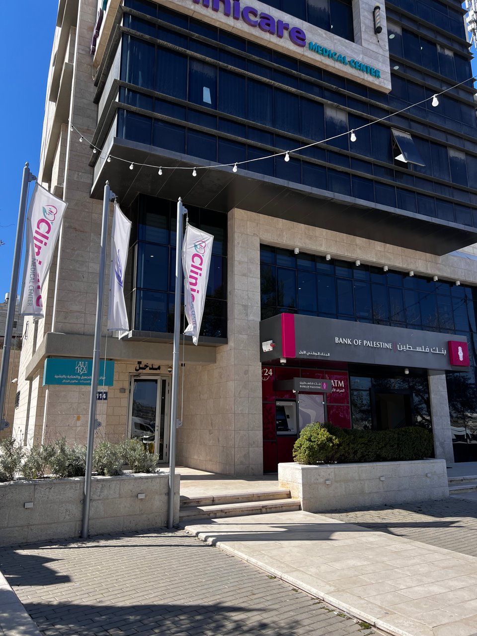 A building entrance with signs for a clinic inside, and the Bank of Palestine