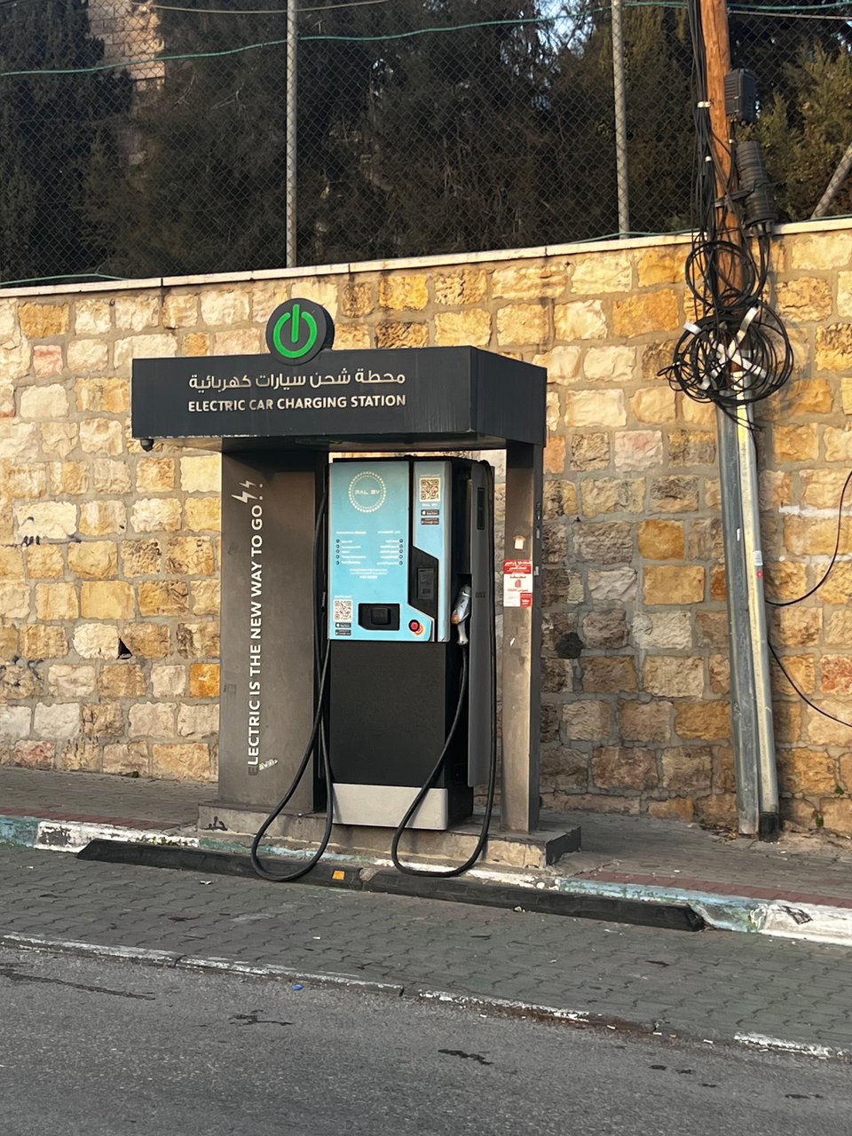 Electric car charging station on the side of a road, in front of a stone wall