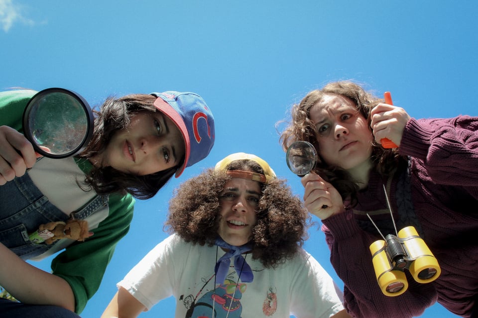 Three girls staring down into the camera, with various investigation tools.